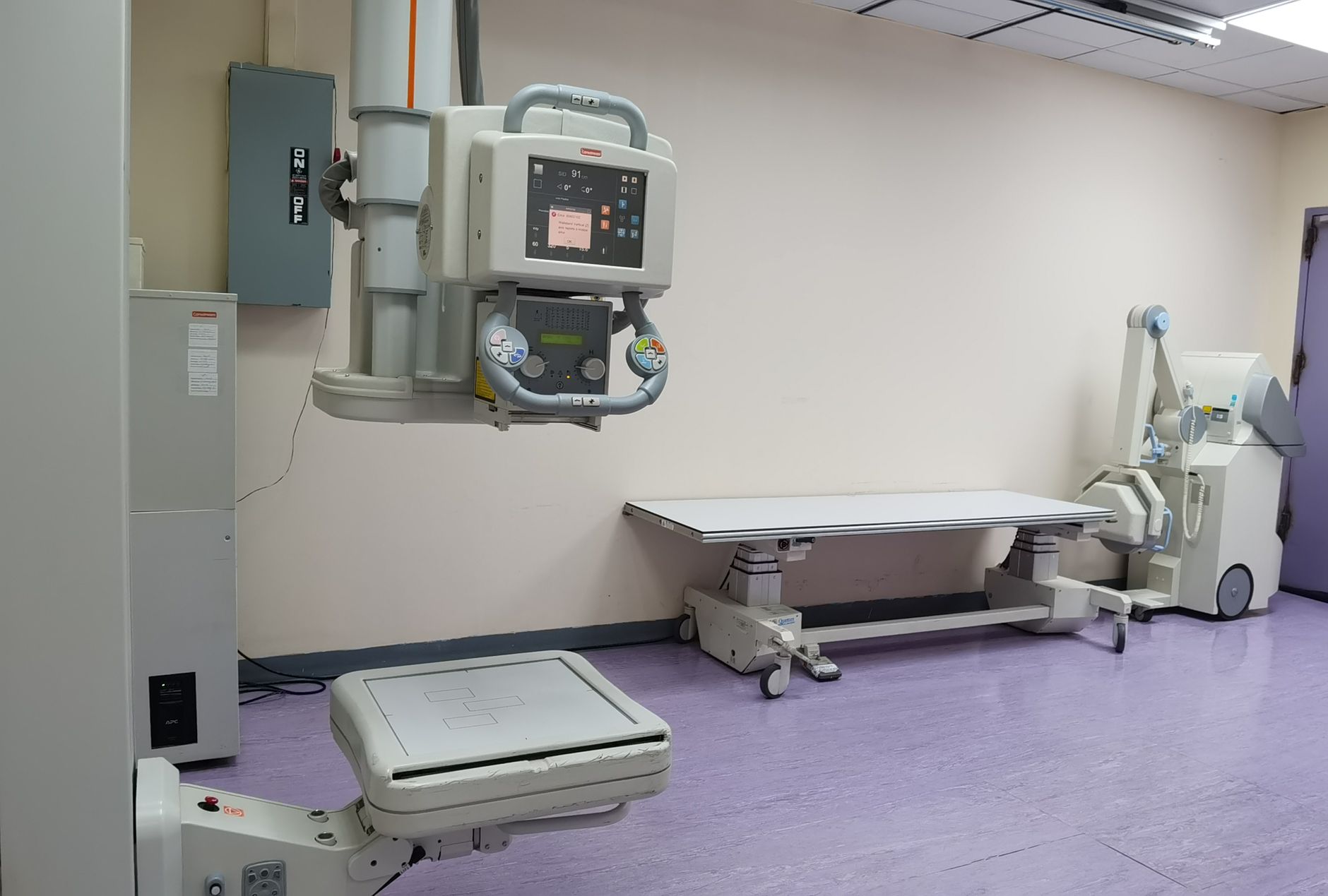 A patient standing in front of a chest X-ray machine in a radiology department