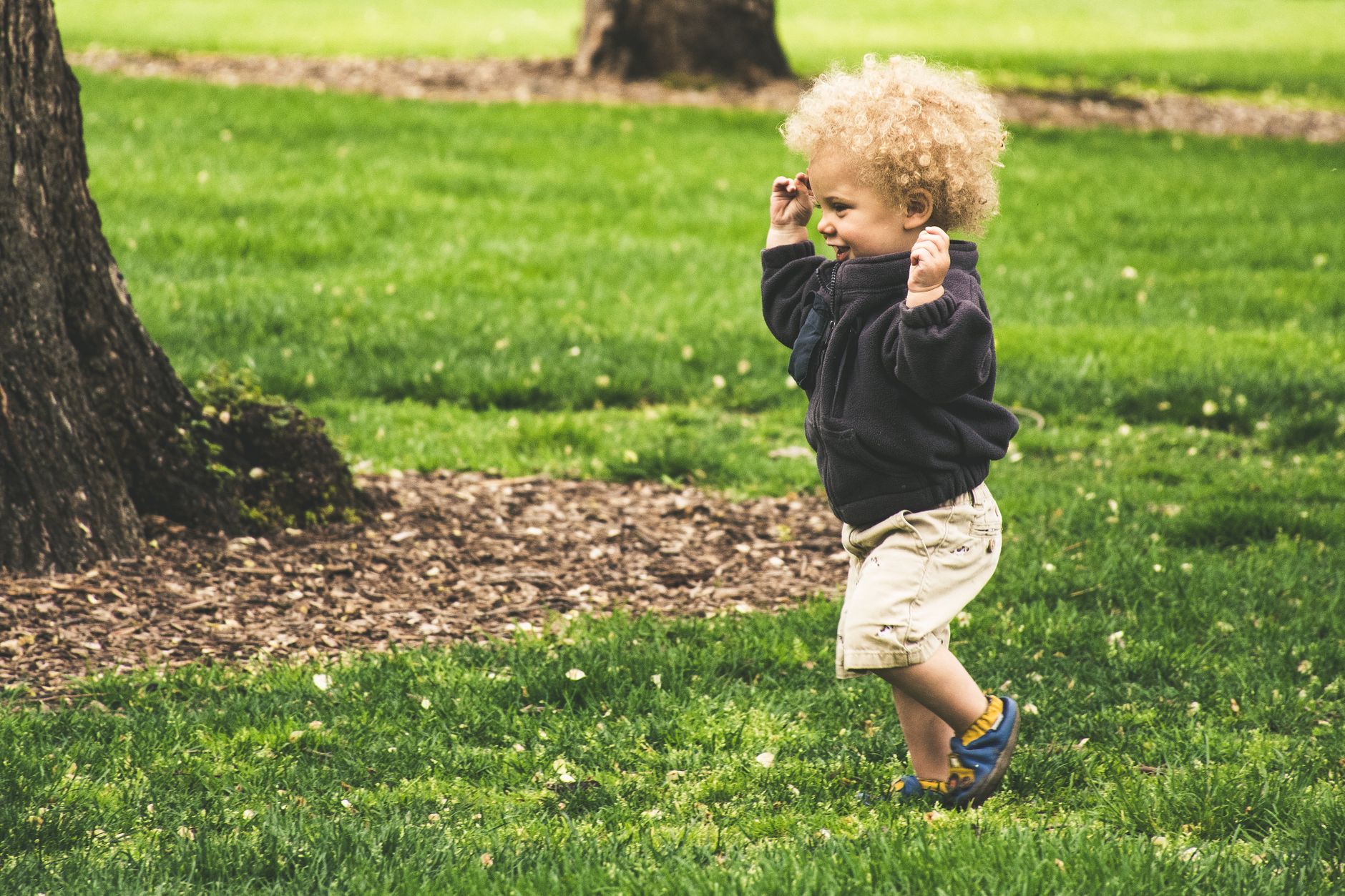 A happy, energetic child running and playing outdoors in a park, representing a healthy active life after heart defect treatment