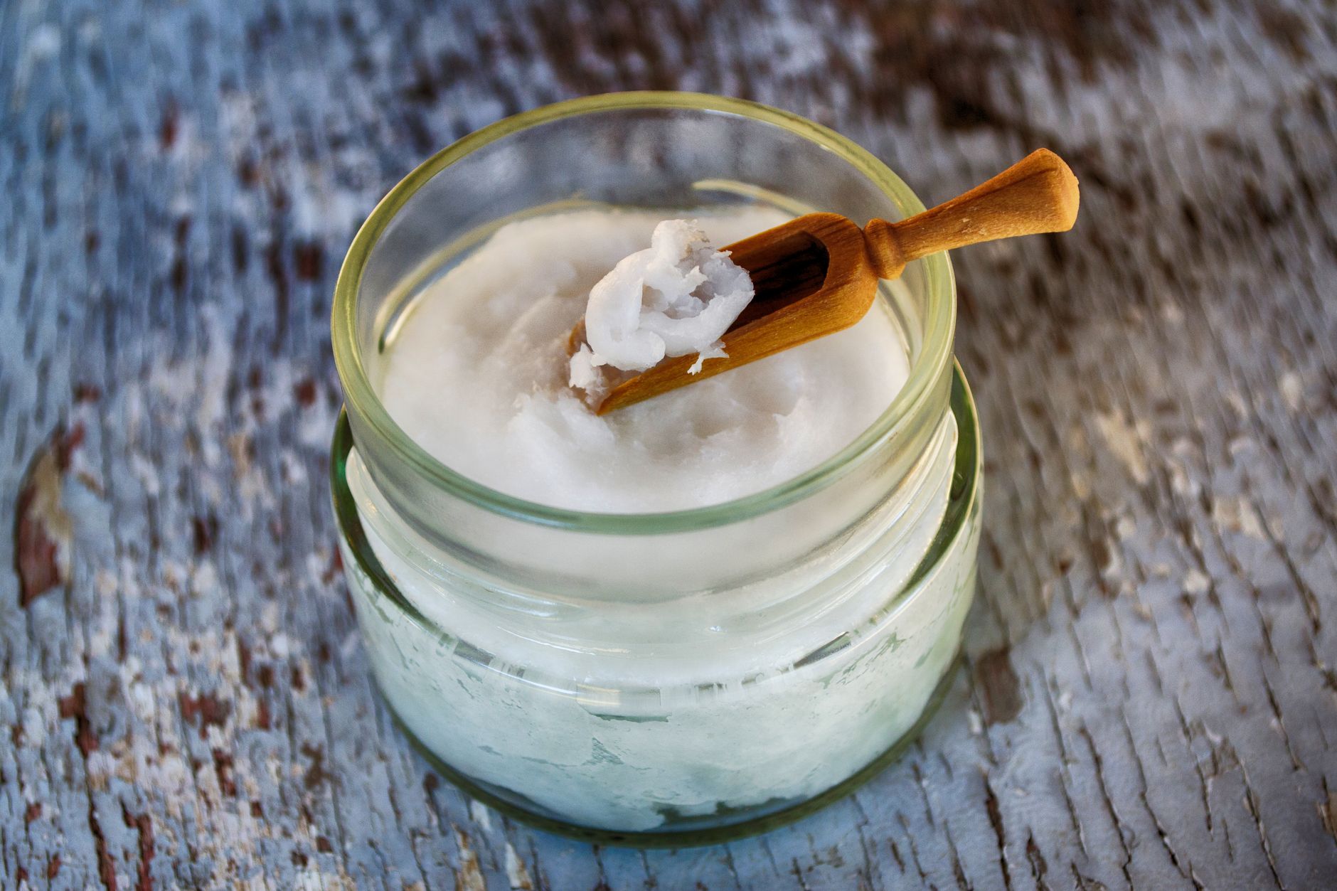 A glass jar of coconut oil beside fresh halved coconuts