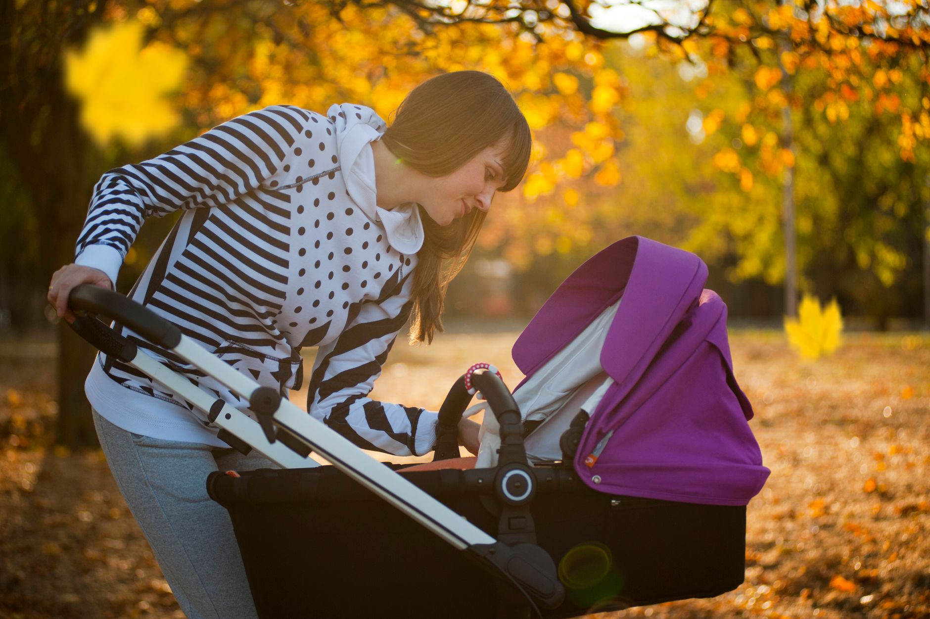 A new mother walking in a park with a baby stroller, promoting postpartum heart health