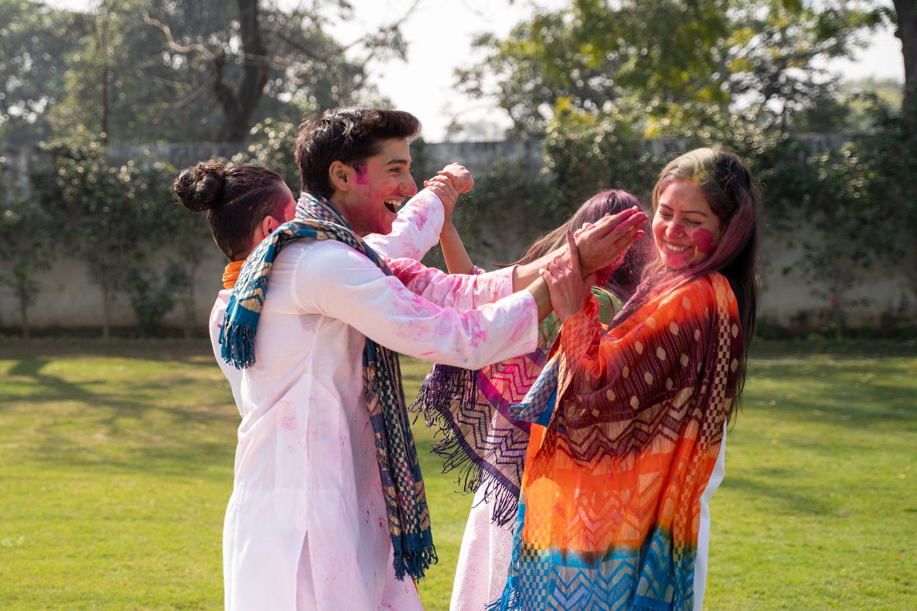 Friends laughing and celebrating Holi outdoors with colourful powder