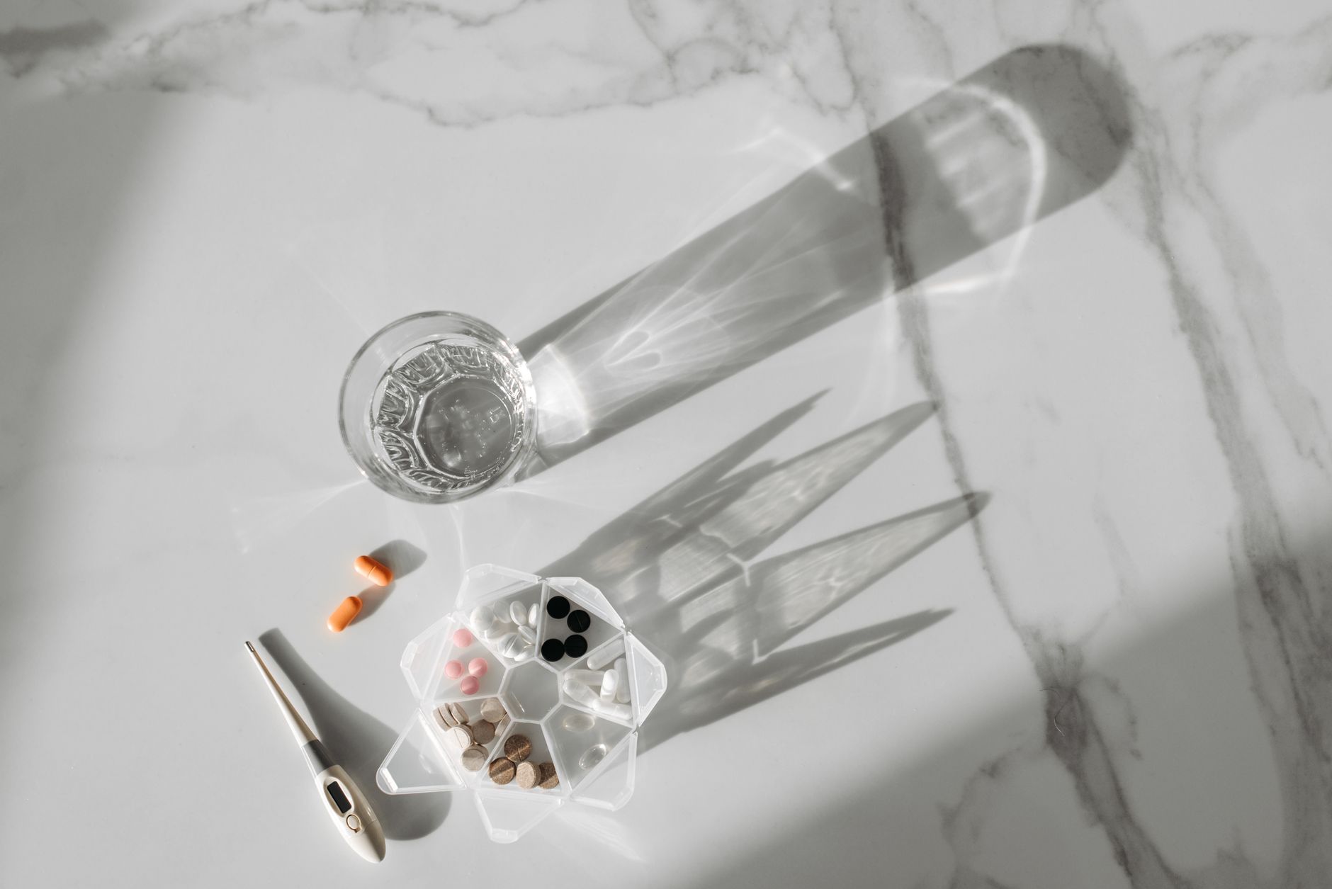 A weekly pill organiser and a glass of water on a wooden table, representing medication management